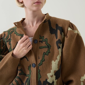Model wearing Urban Aran brown merino wool cardigan with abstract camo intarsia knit pattern and navy button fastening, close-up detail view
