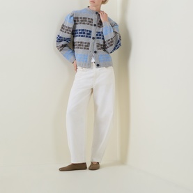 Model wearing Urban Aran grey merino wool cardigan with fair isle pattern, styled with white wide-leg trousers and brown loafers.