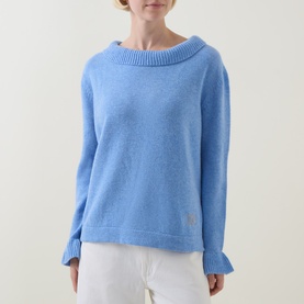 Model wearing Urban Aran blue merino wool knit jumper with wide boat neckline and ribbed cuffs, styled with white trousers