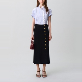 Model wearing Claude Pierlot black midi skirt with gold buttons, styled with a blue striped shirt, burgundy bag and tan sandals.