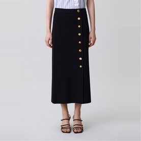 Model wearing Claude Pierlot black midi skirt with gold button detail, styled with a striped top and brown strappy heeled sandals.