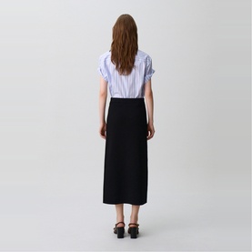 Model wearing Claude Pierlot black midi skirt, styled with a light blue striped shirt and black block-heel sandals, rear view.