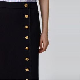 Model wearing Claude Pierlot black midi skirt with gold decorative button front detail, close-up view