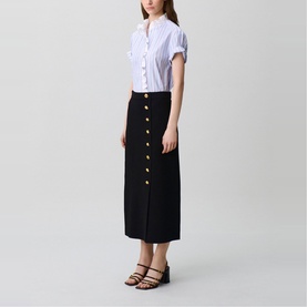 Model wearing Claude Pierlot black midi skirt with gold button-front detail, styled with a striped short-sleeve shirt and black sandals.