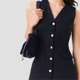 Model wearing Maje Womens French Dress in navy pinstripe, sleeveless V-neck with pearl buttons, styled with a navy shoulder bag