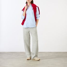 Model wearing Ami Paris grey cotton trousers styled with a light blue shirt and red vest, paired with cream loafers.