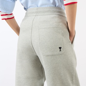 Model wearing Ami Paris grey cotton jogger trousers, rear view showing patch pocket with embroidered heart logo.