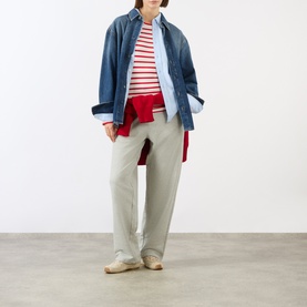 Model wearing Ami Paris grey cotton trousers with red striped top, denim overshirt and cream shoes