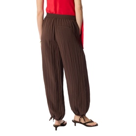 Model wearing Whistles brown wide-leg harem trousers with elasticated waist and tie ankles, styled with a red top.