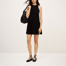 Model wearing Bash black pleated sleeveless mini dress, styled with black strappy flat shoes and carried black quilted hobo bag.