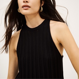 Model wearing Bash black ribbed knit sleeveless top with halter neckline, styled with gold hoop earrings
