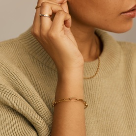 Model with Missoma gold chain-link bracelet, worn with a gold ring, styled with a sage green knit jumper.
