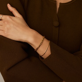 Model with Missoma gold chain-link and snake bracelet stack, worn on wrist over brown ribbed blazer