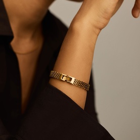 Model with Missoma gold wide mesh bracelet featuring a square buckle clasp, worn on wrist against dark clothing