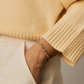 Model with Missoma gold and silver chain-link bracelet, styled with a pale yellow ribbed knit sweater and white trousers