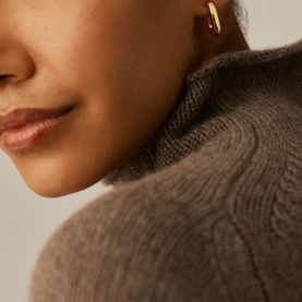 Model with Missoma gold hoop earring, shown close up at ear, styled with a taupe turtleneck jumper