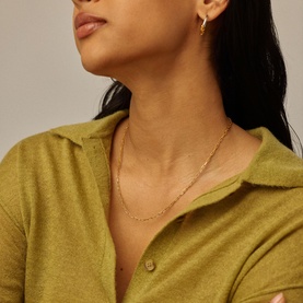 Model with Missoma gold fine chain necklace, styled with matching gold hoop earrings and an olive green knit top.