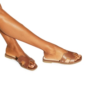 Model wearing KG by Kurt Geiger beige leather flat slides with wide H-bar strap and flat tan sole.