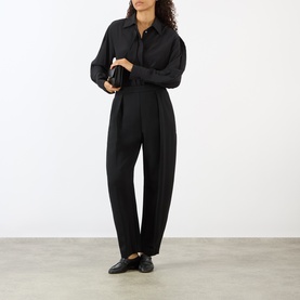 Model wearing Rohe black wide-leg trousers with pleated front, styled with matching black shirt and loafers.