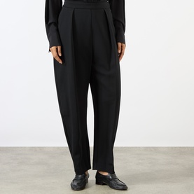 Model wearing Rohe black wide-leg tapered trousers with pleat front detail, styled with black loafers and a black long-sleeve top.