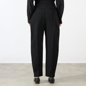 Model wearing Rohe black wide-leg trousers, rear view, styled with a black blouse and black loafers.