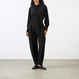 Model wearing Rohe black tailored trousers in viscose blend, styled with a black tie-neck blouse and black loafers.