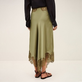 Model wearing Bash green satin midi skirt with lace trim hem, styled with black blouse and black strappy flat sandals