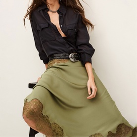 Model wearing Bash Womens French Dress in green with gold lace hem trim, styled with black shirt and woven belt
