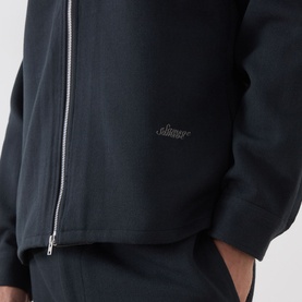 Model wearing Samsoe & Samsoe Dark Grey Mel casual jacket, close-up of silver zip and logo detail, styled with matching trousers.