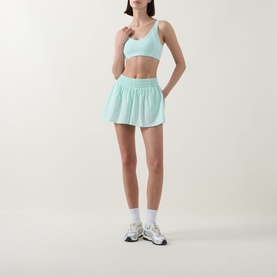 Model wearing Tala SkinLuxe Contrast Piping Sports Bra in Soft Mint, styled with matching mini skirt and white trainers.