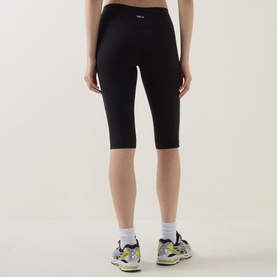 Model wearing Tala Shadow Black cropped knee-length leggings, styled with white ankle socks and multicoloured trainers.