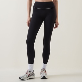 Model wearing Tala Shadow Black leggings with white contrast waistband trim, styled with white socks and grey trainers