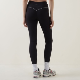 Model wearing Tala Shadow Black leggings, rear view, with reflective trim detailing at waistband, styled with white socks and trainers.