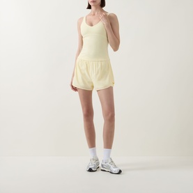 Model wearing Tala SkinLuxe Built-In Two-in-One Shorts in Lemon Yellow, styled with a matching yellow vest top and white trainers.