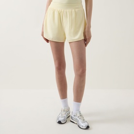 Model wearing Tala SkinLuxe Built-In Two-in-One Shorts in Lemon Yellow, styled with white ankle socks and silver trainers.