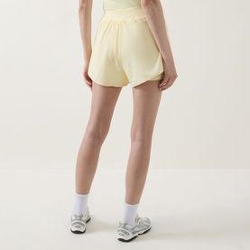 Model wearing Tala SkinLuxe Built-In Two-in-One Shorts in Lemon Yellow, shown from behind, styled with white socks and trainers.