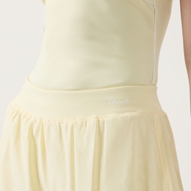 Model wearing Tala SkinLuxe Built-In Two-in-One Shorts in Lemon Yellow, showing elasticated waistband with logo detail and flowy skirt overlay.