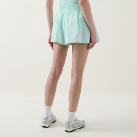 Model wearing Tala SkinLuxe Ruched Floaty Shorts in Soft Mint with white ankle socks and grey trainers, rear view