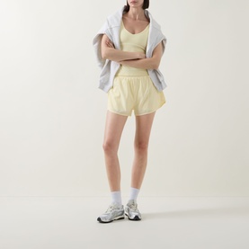 Model wearing Tala SkinLuxe Contrast Piping Tank Top in Lemon Yellow, styled with matching shorts, white socks and grey trainers.