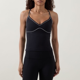 Model wearing Tala top in Shadow Black with white contrast piping, cross-back straps, and fitted silhouette, styled with black leggings