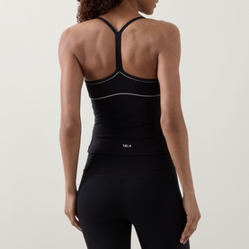 Model wearing Tala top in Shadow Black with white contrast piping and racerback detail, styled with matching black leggings.