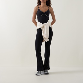 Model wearing Tala top in Shadow Black with white contrast stitching, styled with cream knotted jumper and black flared trousers.