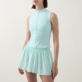 Model wearing Tala SkinLuxe Zip Through Running Top in Soft Mint with matching flared mini skirt. Sleeveless, mock neck, front zip.