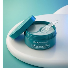 The Skin Nerd Eye-Light Eye-Bright Arbutin Under-Eye Pads in open teal jar with applicator tool on light surface