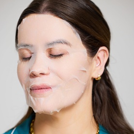 Model wearing The Skin Nerd Hydra-Hit Instant Facial Mask, a translucent sheet mask applied to face, eyes closed