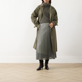 Model wearing Vince light green pleated midi skirt, styled with olive trench coat and grey turtleneck, black ankle boots