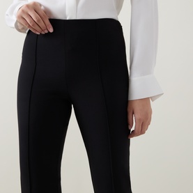 Model wearing Vince black trousers with front seam detail, styled with a white long-sleeve shirt. Close-up of waist and hip area.