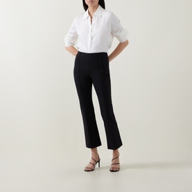 Model wearing Vince black kick-flare trousers with white shirt and black strappy heeled sandals.