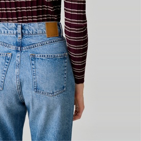 Model wearing Claude Pierlot Straight Leg Jeans in blue denim, showing rear view with leather jacron patch and silver rivets, styled with a striped