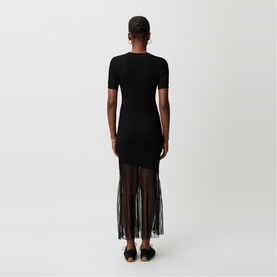 Model wearing Claude Pierlot black short-sleeve fitted dress with sheer mesh fringe hem, back view, paired with black flat sandals.